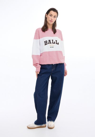Rosa og hvit fargeblokkert hettegenser med "BALL" trykt i svart; tilpasset løstsittende mørkeblå jeans og hvite joggesko.