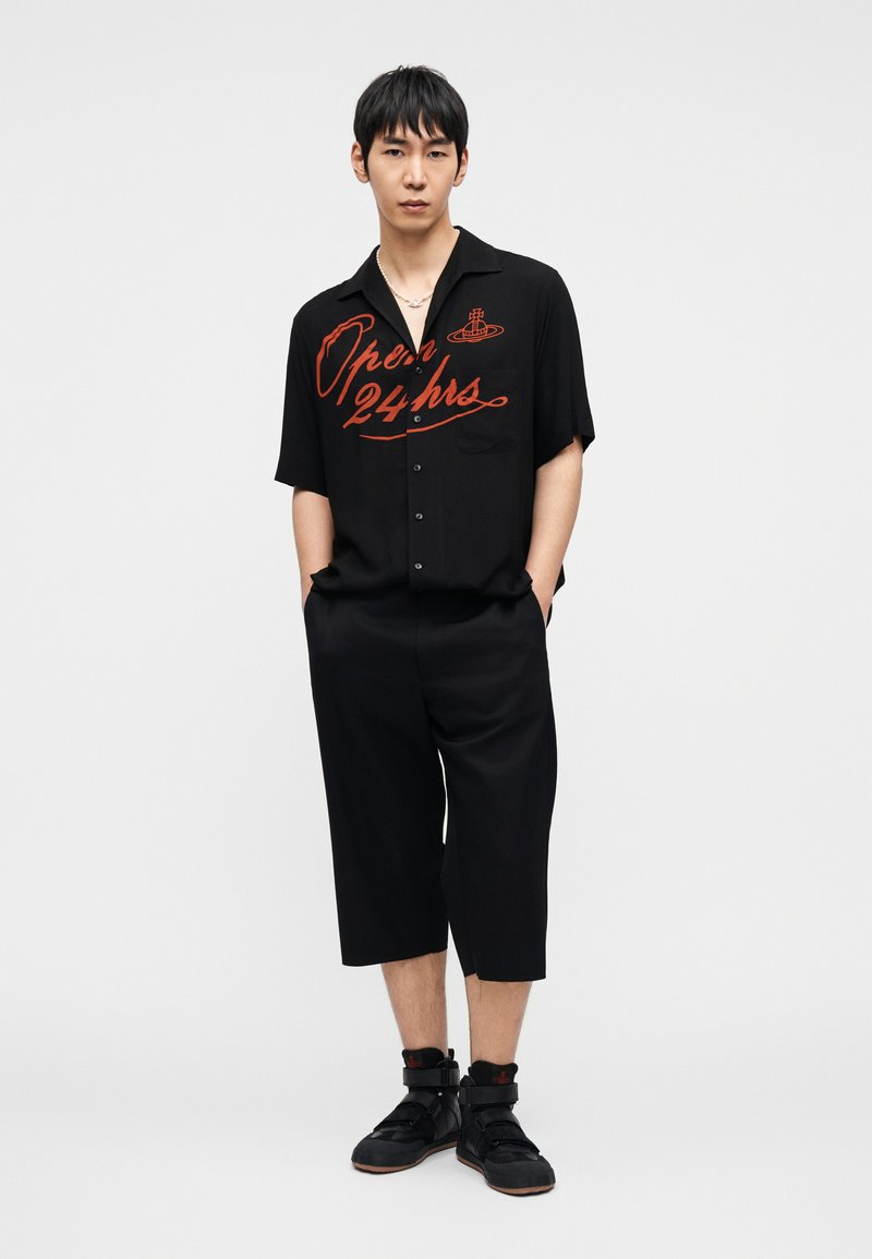 Chemise noire à manches courtes avec texte graphique rouge, associée à un pantalon noir jusqu'aux genoux et des baskets montantes noires avec des sangles.