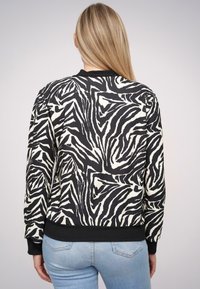 Czarny i biały sweatshirt w zebrę z okrągłym dekoltem, elastycznymi mankietami i dołem. Materiał wydaje się gładki z lekko błyszczącym wykończeniem.