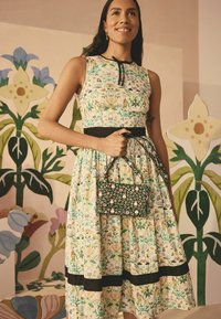 Floral-patterned dress with a fitted bodice and flared skirt, featuring a black waistband. Woven black handbag with colorful floral accents.
