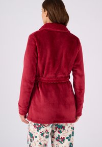Accappatoio di pile rosso con colletto a scialle, cintura integrata e maniche lunghe. Il materiale appare morbido con una texture liscia e di un colore uniforme.