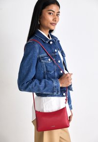 Borsa a tracolla rossa in pelle con una texture liscia, parte superiore arrotondata e hardware in argento. La tracolla è regolabile per maggiore versatilità.