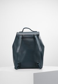 Ciemnozielony skórzany plecak o zaokrąglonym kształcie, z górnym uchwytem i regulowanymi paskami. Gładka tekstura i minimalistyczny design bez wzorów.