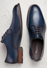 Zapatos de cuero azul marino con cordones, punta redondeada, cordones marrones y un detalle en el tacón marrón texturizado, que muestran un acabado suave y un diseño elegante.