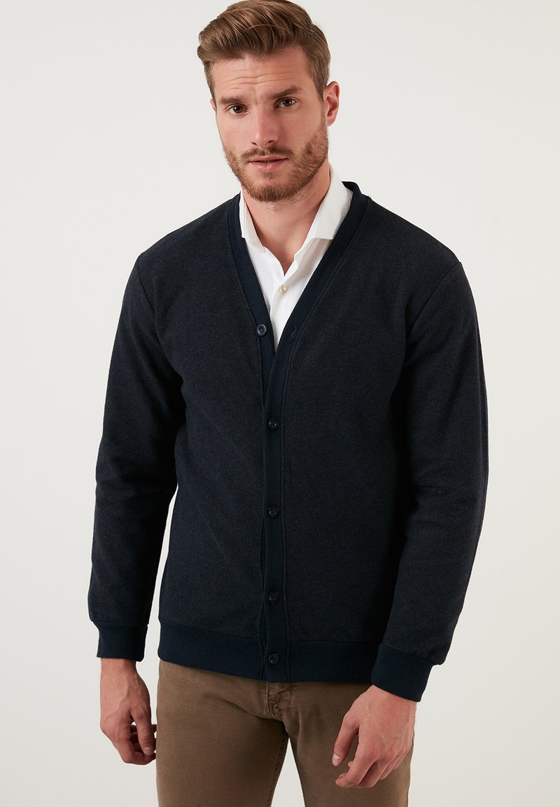 Jūras spēku adīta kardigāna jakas ar V veida kakla izgriezumu, kontrastējošu apmalīti un pogu aizdari. Struktūrai ir ribotas piedurknes un apakša, izgatavota no mīksta auduma.