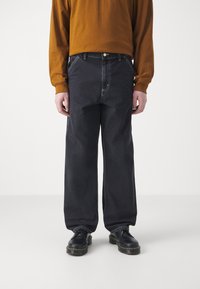 Mørke denim vide bukser med framlommer, kontrasterende hvit søm og knappelukking, sammen med en brun langermet skjorte.