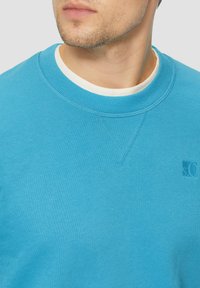 Türkiser Sweatshirt mit Rundhalsausschnitt, geripptem Kragen und Logodetail. Hergestellt aus weichem Material mit glatter Textur.