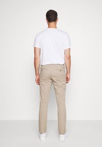 Beige chinos med två bakfickor och knappstängningar; parat med en enkel vit t-shirt med kort ärm, bärs med vita sneakers.