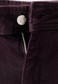 Temno vijolične jeans hlače iz jeansa z odklenjenim srebrnim zadrgo in srebrnim gumbom z gravuro "MNG Jeans" blizu pasu.