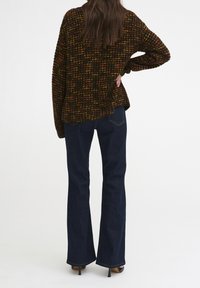 Maglione lavorato a maglia con motivo testurizzato multicolore, abbinato a jeans a zampa d'elefante blu scuro, con dettagli sull'orlo e scarpe con tacco alto.