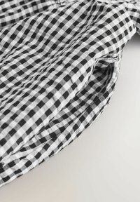 Tissu à carreaux noir et blanc plié pour montrer une couture ou un détail de bord incurvé sur un fond clair.