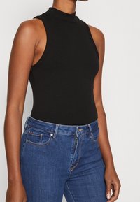 Body negro de canalé sin mangas con un cuello alto, combinado con pantalones vaqueros de denim azul que presentan un diseño clásico de cinco bolsillos y costuras sutiles.