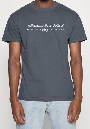 Dark gray short-sleeve shirt with white "Abercrombie & Fitch Established New York, NY" text and moose logo worn by person in light blue jeans.