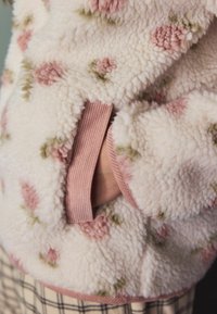 Uldet jakke med pink og grønne blomster mønstre. Har ribbede pink detaljer og sidelommer. Blød, tekstureret overflade.