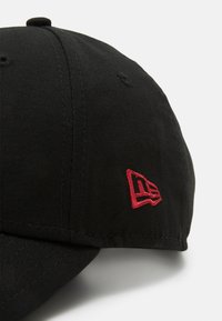 Boné de basebol preto com aba curva, feito de tecido, apresentando um logótipo bordado vermelho na lateral. Textura suave com detalhes em costura.