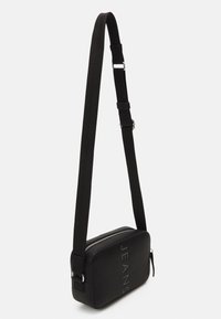 Borsa a tracolla rettangolare nera con finitura testurizzata, dotata di testo in rilievo "JEANS" e tracolla regolabile. Chiusura con zip.