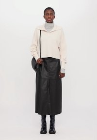 Lys beige cropped genser med bred krage, lagd over en tettsittende grå høyhalset genser. Svart fuskeskinn maxi skjørt og ankel støvler.