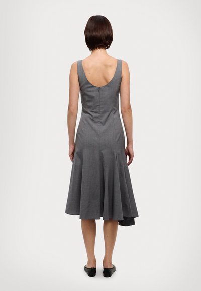 Rochie gri, până la genunchi, cu fustă cloș, spate decupat și panouri laterale decorative. Materialul pare neted, cu o textură subtilă. Pantofi negri, fără toc.