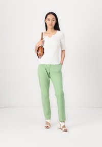 White ribbed short-sleeve top with scalloped edges, paired with light green pants and white heeled sandals. Brown bag slung over the shoulder.