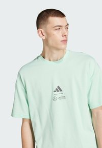 Tirkizna pamučna majica kratkih rukava, sivi Adidas logo i Mercedes brending na prsima. Standardna kroja.