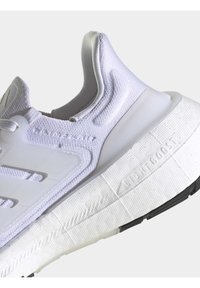 Witte sportschoen met een gestructureerde bovenkant, mesh-details en een dikke zool met een contrasterende zwarte grip. Opvallende merklogo aan de zijkant.