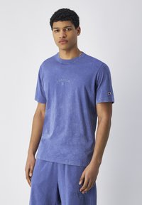 Blauwe crew neck t-shirt van zacht materiaal met een vervaagde was, met in het midden het "Champion" logo en een klein logo op de mouw.