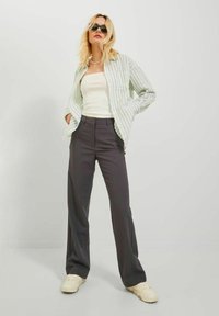 Camisa de botones a rayas verde claro sobre una camiseta sin mangas blanca, combinada con pantalones oscuros grises y zapatillas crema, con un ajuste relajado y una textura suave.