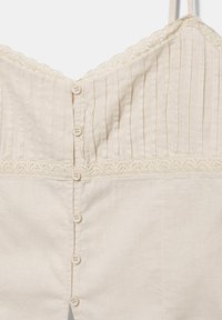 Haut sans manches couleur crème avec des rayures verticales sur la partie supérieure, bordure en dentelle le long de la poitrine et de l'ourlet, et une rangée de boutons sur le devant.