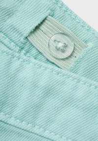 Lichtblauwe denimstof met zichtbare stiksels, een knoopsluiting en gestructureerde stiksels op het label. Glad oppervlak met een licht versleten uiterlijk.