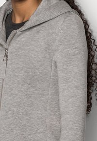 Felpa grigia con zip, realizzata in tessuto morbido e strutturato, con cappuccio e cerniera metallica. Il design comprende tasche laterali e una vestibilità comoda.