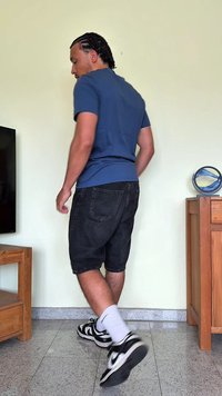 Μπλε κοντομάνικο μπλουζάκι, μαύρες τζιν βερμούδες και μαύρα-άσπρα αθλητικά παπούτσια. Σταθείτε σε πλακάκι κοντά σε ξύλινα έπιπλα.