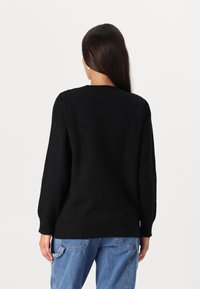 Pull en tricot noir avec des manches longues, un col rond et un ourlet côtelé. Le tissu semble doux et texturé, présentant une coupe décontractée.