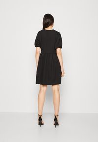 Vestido negro con un corsé ajustado, mangas abullonadas y una falda acampanada. Combinado con zapatos de tacón alto negros. Diseño minimalista y textura suave.