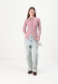Cardigan rosa canelado de mangas longas com colarinho e fecho de botão, combinado com jeans de cintura alta azul claro e uma pequena bolsa lavanda.