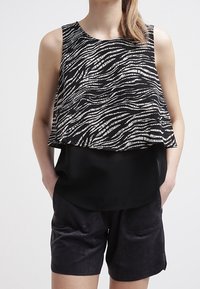 Top senza maniche bianco e nero con un motivo a strisce ondulate, design a strati, abbinato a pantaloncini in suede neri con tasche laterali.