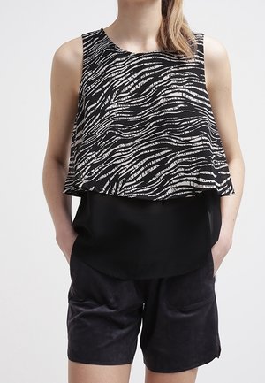 Top senza maniche bianco e nero con un motivo a strisce ondulate, design a strati, abbinato a pantaloncini in suede neri con tasche laterali.