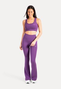 Brassière de sport violette et leggings évasés en tissu extensible. Texture lisse avec une coupe ajustée. Détail de logo subtil sur les deux pièces.