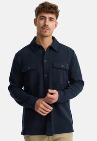 Chemise boutonnière bleu marine en tissu texturé ; dotée de deux poches poitrine et d'un col, avec des manches longues et un ourlet droit.