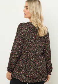 Schwarze Bluse mit langen Ärmeln, die eine enge Taille, geraffte Bündchen und ein Muster aus rosa und grünen Blumen auf dunklem Hintergrund aufweist.