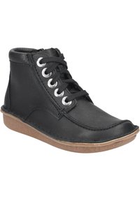 Botas de tobillo de cuero negro con ojales de metal, cordones negros y una suela de goma texturada en marrón; diseño elegante con punta redondeada.