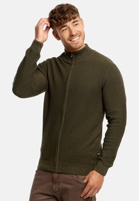 Sudadera de cremallera en verde oscuro con cuello alto, tela texturada y mangas ajustadas. Cuenta con una cremallera frontal completa y detalles acanalados.