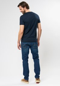 Tumesinine puuvillane T-särk ümarate kraega, koos pleekinud siniste teksade ja tan värvi vabaaja kingadega; nähtavad kangatekstuur ja õmbluse detailid.