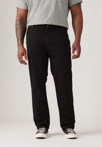 Zwarte denim jeans met een rechte pijp, vijf zakken en een voorknoopsluiting. Draag met een grijs t-shirt en met een patroon bedekte sneakers.
