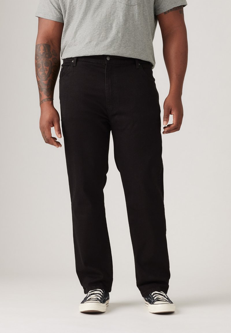 Zwarte denim jeans met een rechte pijp, vijf zakken en een voorknoopsluiting. Draag met een grijs t-shirt en met een patroon bedekte sneakers.