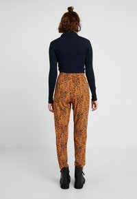 Námornický rolák v kombinaci se vzorovanými, vysokými kalhotami v hnědé barvě s černými skvrnami a černými kotníkovými botami. Matný povrch, přiléhavý střih.