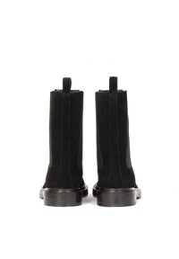 Par de botas de tobillo de ante negro con tiradores y tacones bajos, mostradas desde atrás sobre un fondo blanco.