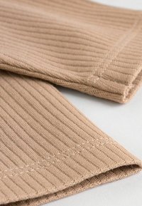 Beiger gerippter Stoff mit einem strukturierten Muster, das sichtbare Nähte und umgeschlagene Kanten aufweist. Weiches, gestricktes Material ohne weitere Verzierung.