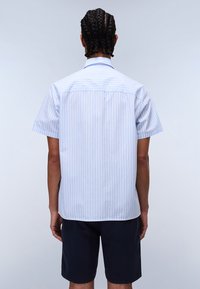 Chemise à manches courtes bleu clair avec des rayures blanches verticales, dotée d'un col standard et d'un empiècement au dos, portée avec un short sombre.