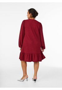 Burgundijas krāsas kleita līdz ceļgaliem ar puffa garajām piedurknēm un ķīļveida apakšmalu. Izgatavota no teksturēta auduma, valkāta ar sudraba augstpapēžu kurpēm.