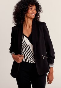 Veste noire avec une coupe ajustée, dotée d'une poche zippée, assortie à un haut blanc arborant de larges rayures noires et un décolleté en V.